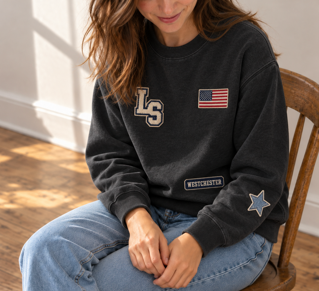 Woman wearing a black patch crewneck with Westchester, American flag, star and monogram patches