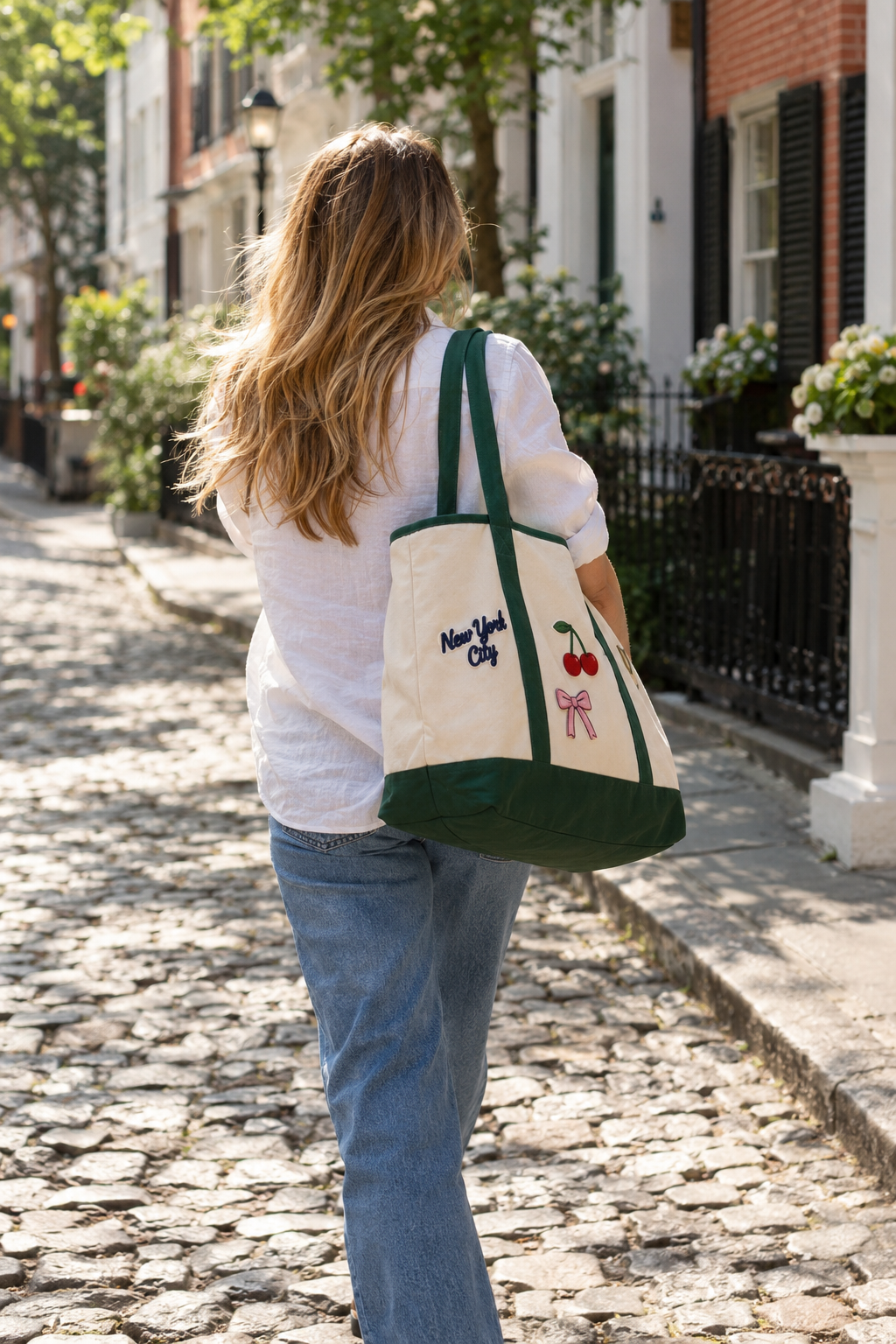 Woman walking a cobblestone street carrying a custom patch tote bag in natural and green