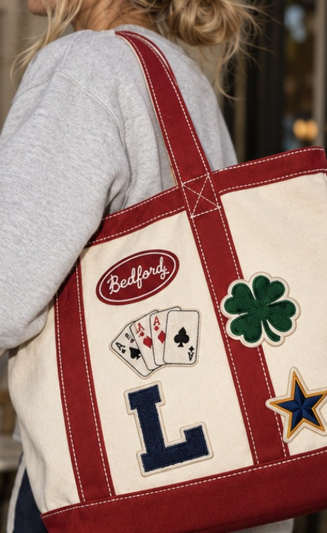 Woman carrying The Bedford Tote in Natural & Red with Bedford, four aces, clover, L letter and star patches